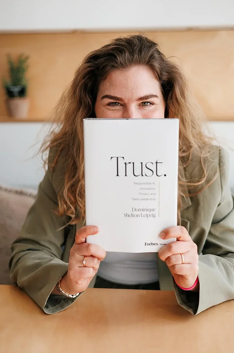 Eine Frau mit welligem Haar hält ein Buch mit dem Titel "Vertrauen" in der Hand. von Dominique Shelton Lepzig.